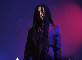 Skip Marley poses in a bold striped suit on a purple and red background to promote the release of his new single “In Our Sight” and official video, filmed in Jamaica.