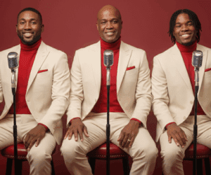 Robert Bailey seated with his sons Joel and Renaldo in coordinated cream suits and red turtlenecks, posing with vintage microphones.
