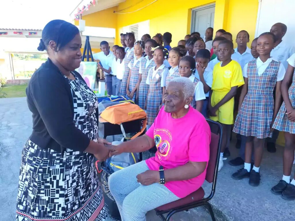 Retired Antiguan educator Teacher Gen being honored at Potters Village as students and community members look on.