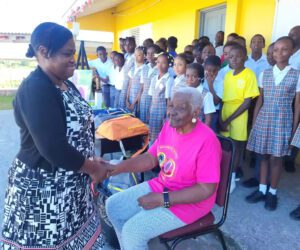 Retired Antiguan educator Teacher Gen being honored at Potters Village as students and community members look on.