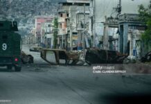 A walks past cars burned by armed gangs and used as a barricade during clashes last week with Haitian security forces on a deserted street in the city center, seen from an armored police vehicle during a patrol, in Port-au-Prince on January 16, 2026. An