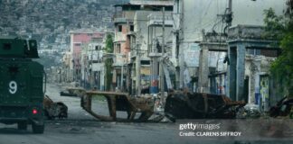 A walks past cars burned by armed gangs and used as a barricade during clashes last week with Haitian security forces on a deserted street in the city center, seen from an armored police vehicle during a patrol, in Port-au-Prince on January 16, 2026. An