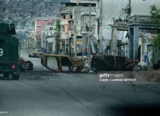 A walks past cars burned by armed gangs and used as a barricade during clashes last week with Haitian security forces on a deserted street in the city center, seen from an armored police vehicle during a patrol, in Port-au-Prince on January 16, 2026. An